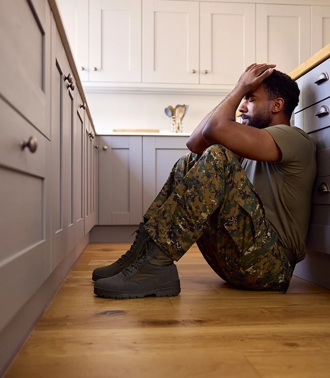 man in military uniform sitting on the floor in a kitchen holding his head from stress, anxiety, ptsd, or otherwise in a mental health crisis